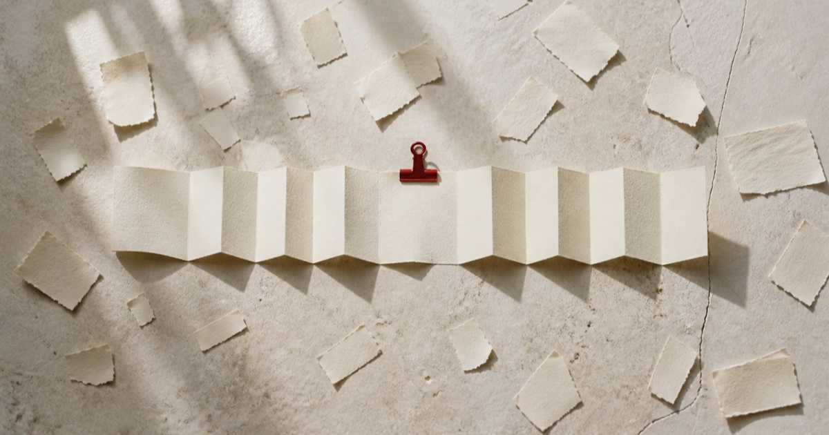 A continuous folded paper strip held by a cinnabar clip, surrounded by scattered scraps of paper